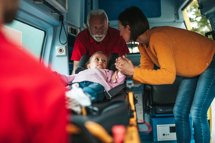 Child lying on ambulance stretcher with concerned adults nearby, illustrating advice kids were given and manipulation realization.