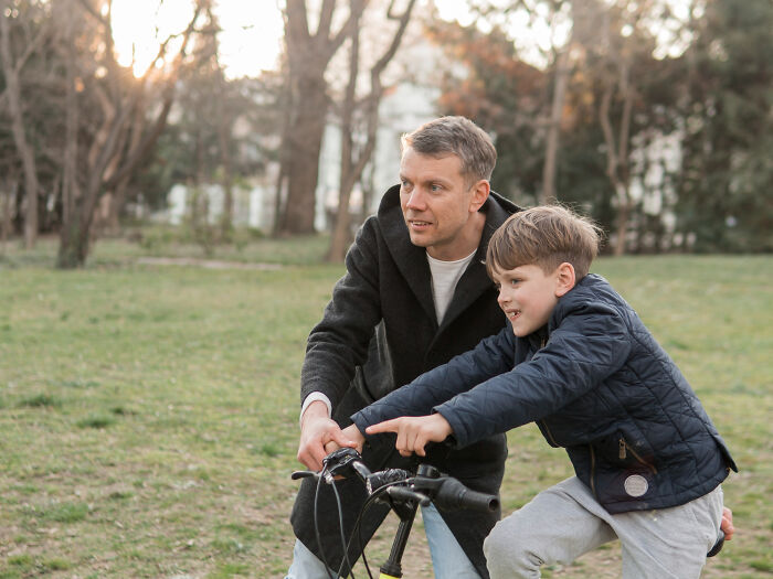 Father teaching son to ride bike outdoors, capturing moments of advice and manipulation in disguise with kids.