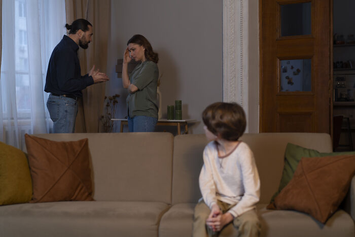 Child sitting on couch looking at parents having a tense argument, illustrating advice kids later realized was manipulation.