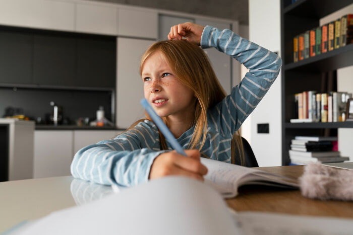 Young girl at a desk looking confused while writing, representing kids realizing manipulation in advice later in life.