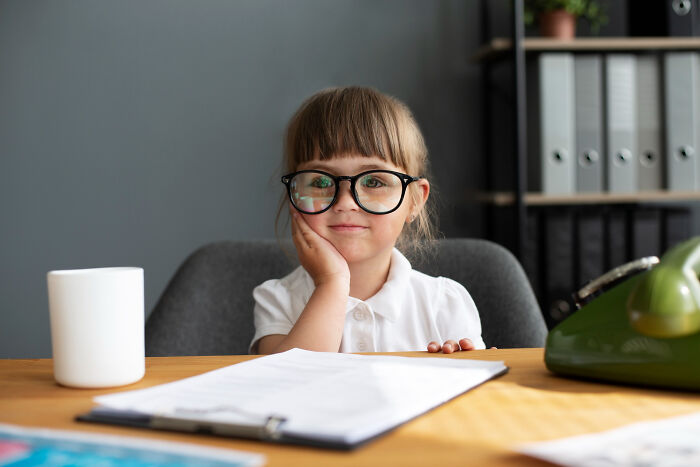 Young girl wearing glasses, sitting at desk with papers, representing advice kids were given and manipulation in disguise.