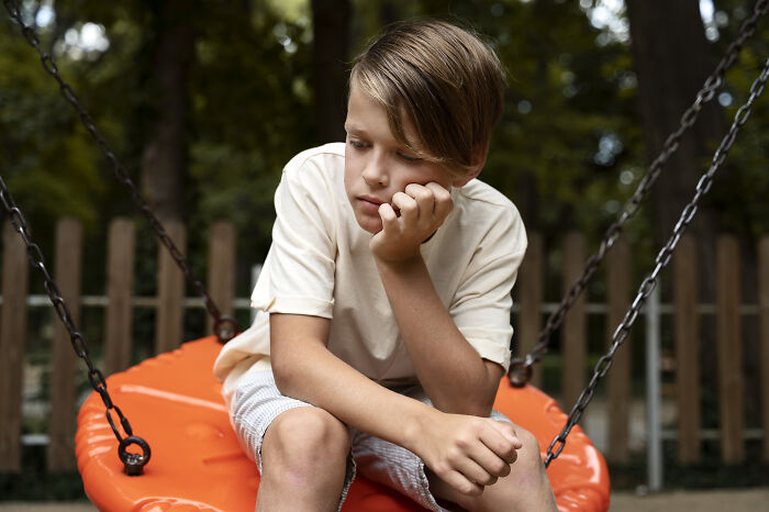 Sad boy sitting alone on orange swing at playground reflecting on advice kids were given and manipulation in disguise.