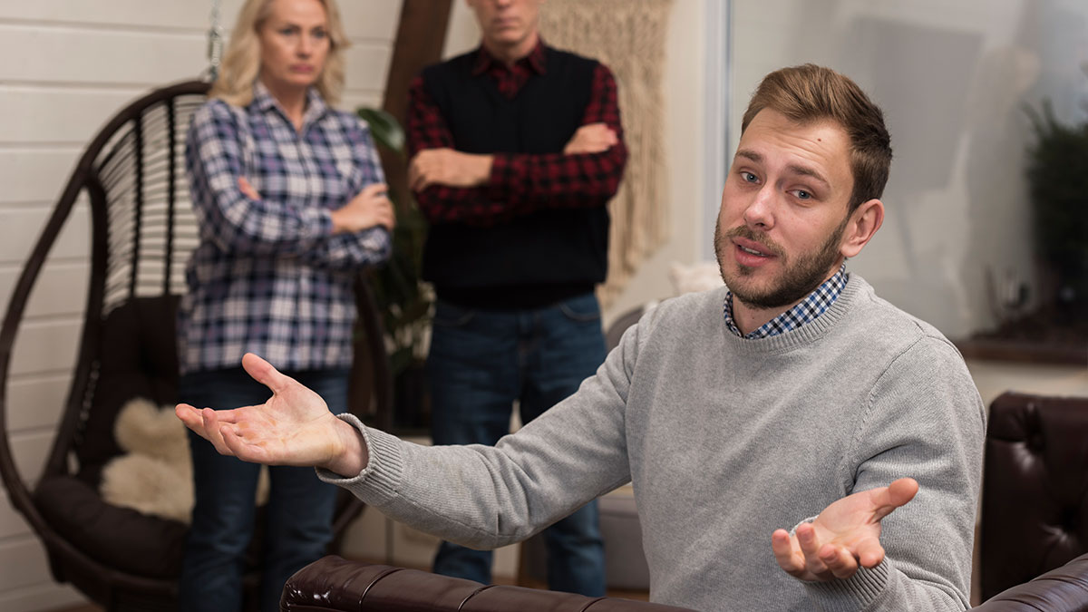 Man explains wedding relocation refusal to upset family members in a living room, sparking family drama over stepsister.