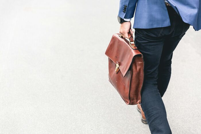 Person in blue suit walking on street, holding a brown leather briefcase, symbolizing revenge on bosses.