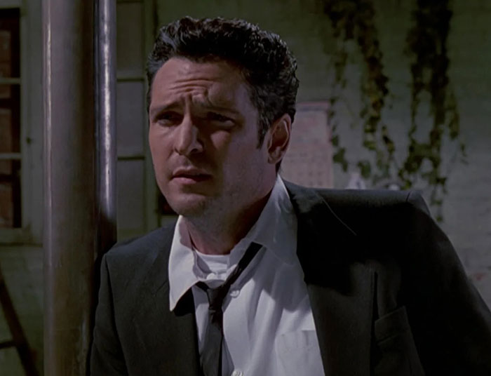 Actor Michael Madsen in a dark suit, looking contemplative with a serious expression in a dimly lit outdoor setting. Actor Michael Madsen in a dark suit, looking contemplative with a serious expression in a dimly lit outdoor setting.
