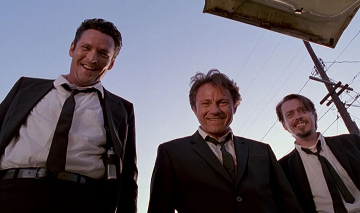 Three men in black suits and ties smiling while standing outdoors under a clear sky, related to actor Michael Madsen tribute. Three men in black suits and ties smiling while standing outdoors under a clear sky, related to actor Michael Madsen tribute.