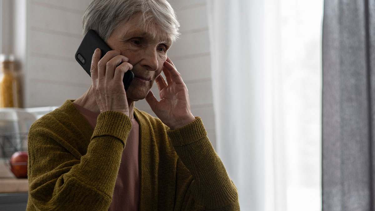 Older woman in a cardigan speaking on the phone, looking concerned, related to custody and false CPS reports.
