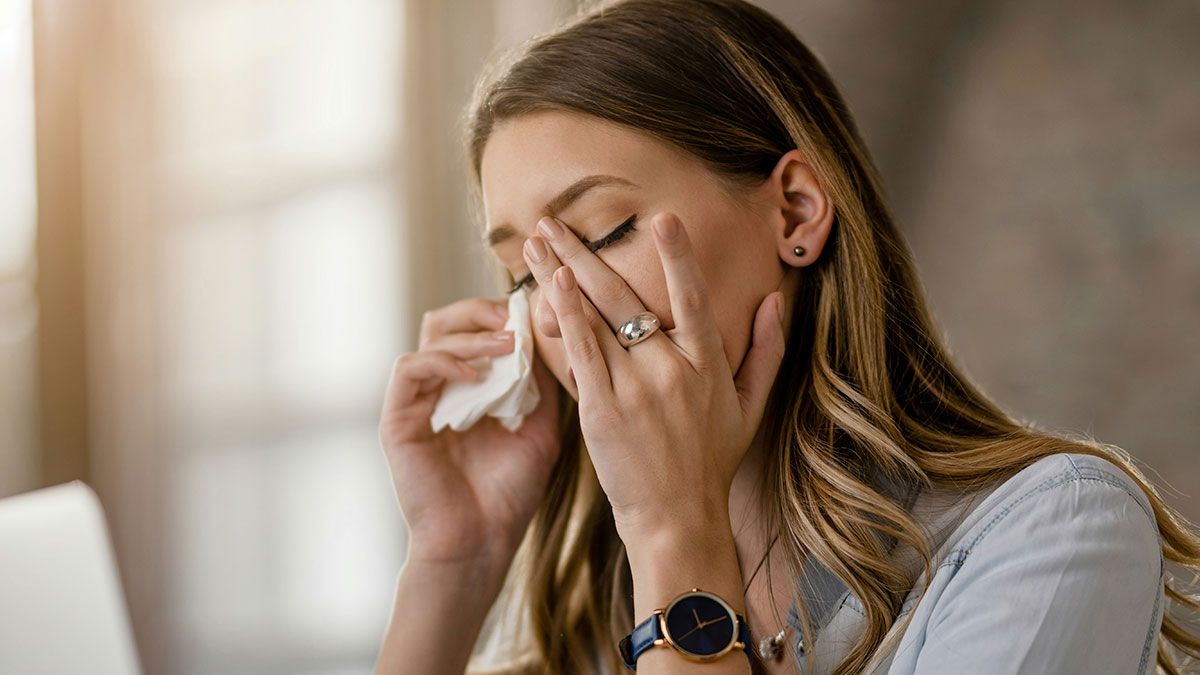 Woman battling cancer wiping tears with tissue, showing emotional distress in a softly lit indoor setting.