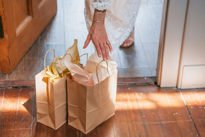 Woman in a white dress reaching for paper bags on wooden floor, illustrating nosy MIL opening others’ packages concept. Woman in a white dress reaching for paper bags on wooden floor, illustrating nosy MIL opening others’ packages concept.