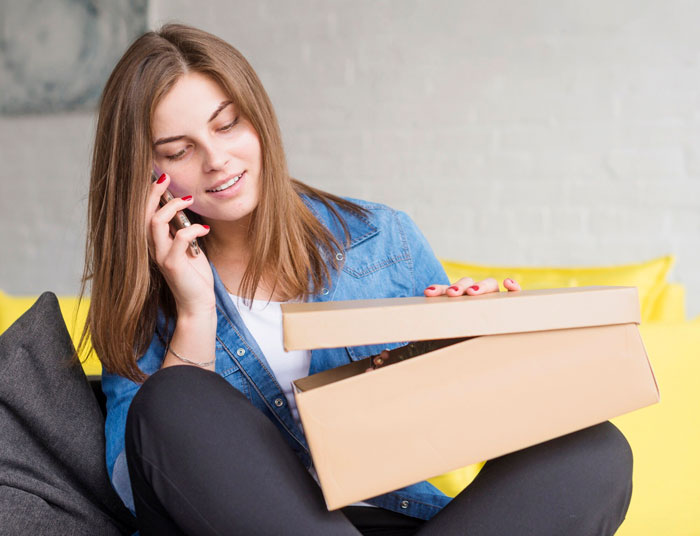 Young woman talking on phone while opening a package, illustrating nosy MIL and vibrating surprise story. Young woman talking on phone while opening a package, illustrating nosy MIL and vibrating surprise story.