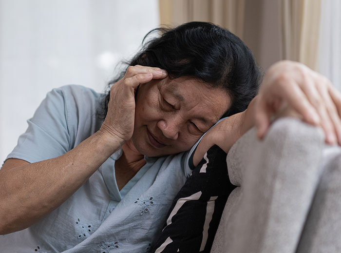 Elderly woman looking distressed on a couch, reflecting family drama involving grandson’s ashes and entitled grandma actions.