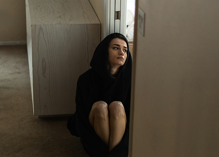 Woman in black hoodie sitting on floor looking away, reflecting on conflict with unhinged stepfather. Woman in black hoodie sitting on floor looking away, reflecting on conflict with unhinged stepfather.