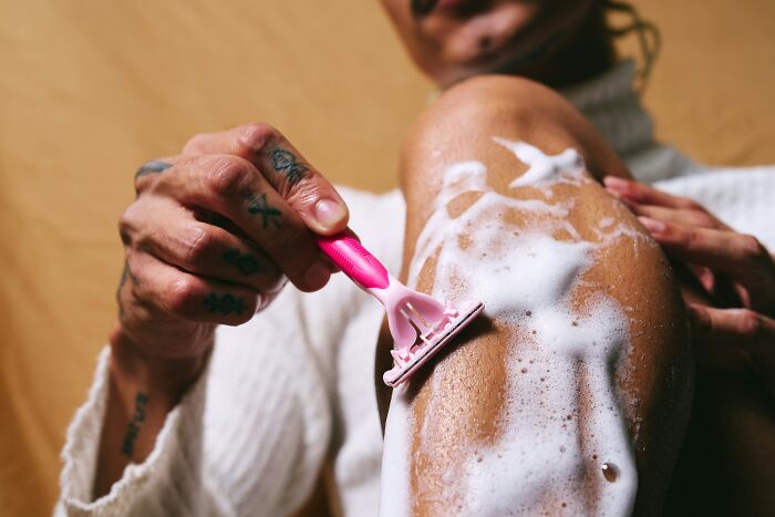 Person with tattoos shaving their leg with a pink razor covered in foam, illustrating common debunked lies people believe.