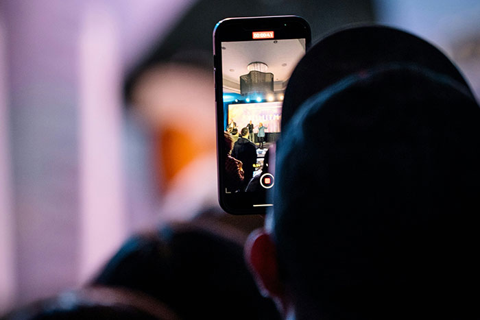 Person recording event on smartphone, illustrating man facing legal consequences as a deadbeat dad in public setting Person recording event on smartphone, illustrating man facing legal consequences as a deadbeat dad in public setting
