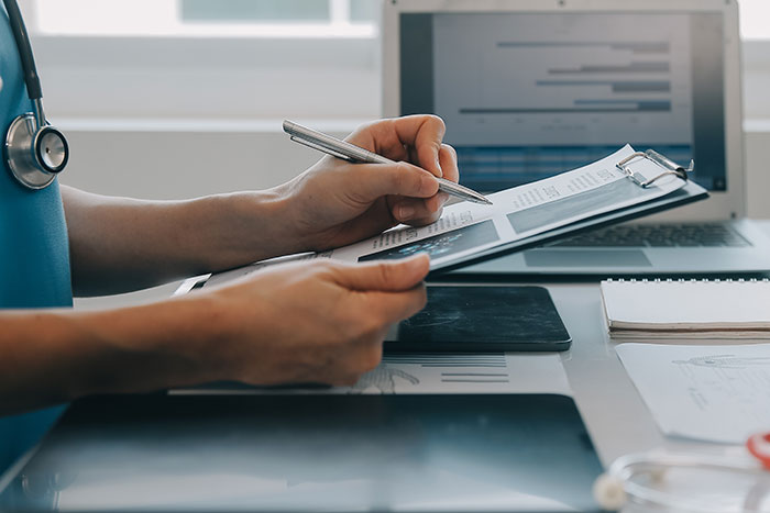 Man reviewing legal documents related to deadbeat dad consequences, holding pen and clipboard near laptop and medical tools. Man reviewing legal documents related to deadbeat dad consequences, holding pen and clipboard near laptop and medical tools.