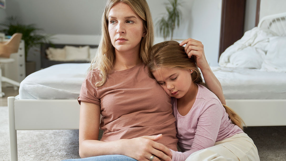 Woman comforting her daughter at home, reflecting emotional strain linked to a man facing deadbeat dad legal issues.