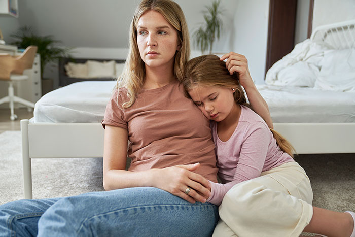 Woman looking concerned while sitting on the floor with her daughter, depicting struggles of a deadbeat dad legal consequences. Woman looking concerned while sitting on the floor with her daughter, depicting struggles of a deadbeat dad legal consequences.