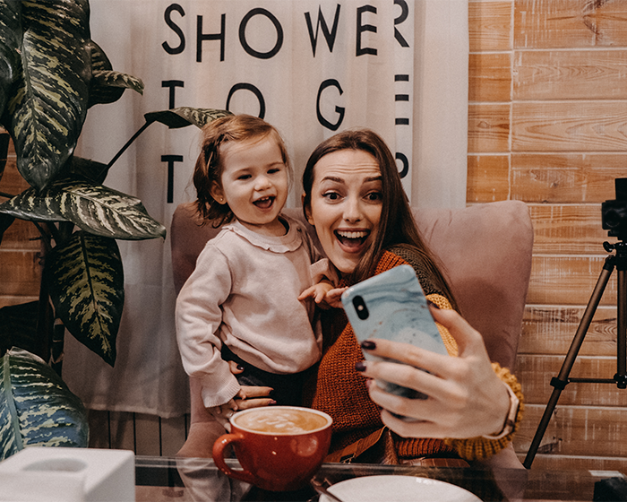 Momfluencer and daughter taking a staged selfie indoors facing backlash for pretend life and online fame pursuit. Momfluencer and daughter taking a staged selfie indoors facing backlash for pretend life and online fame pursuit.