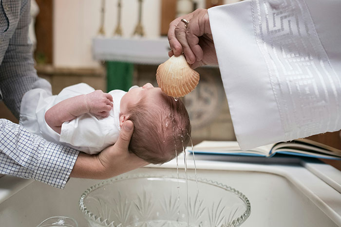 Baby being christened in a church as part of a Christian naming ceremony amid family disagreement.
