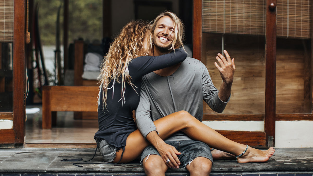Couple enjoying a stress-free trip before wedding, sitting together and embracing in casual summer clothes.
