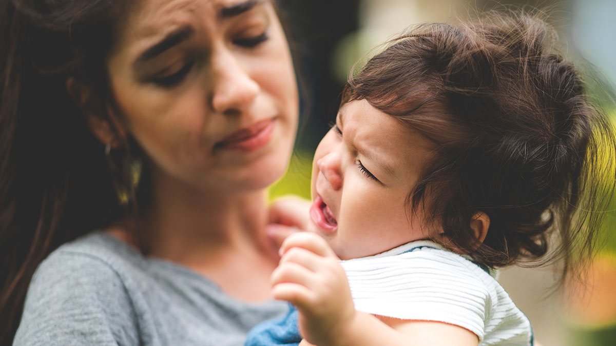 Mother looking distressed while holding crying toddler, capturing honest emotions in a mom and child moment.