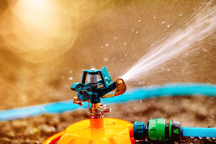 Garden sprinkler spraying water on soil near driveway with blocked neighbor truck causing petty revenge. Garden sprinkler spraying water on soil near driveway with blocked neighbor truck causing petty revenge.