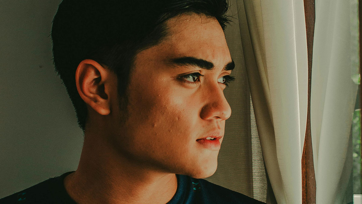 Young man looking out a window, upset while ranting about neighbor and farm stand theft issues.