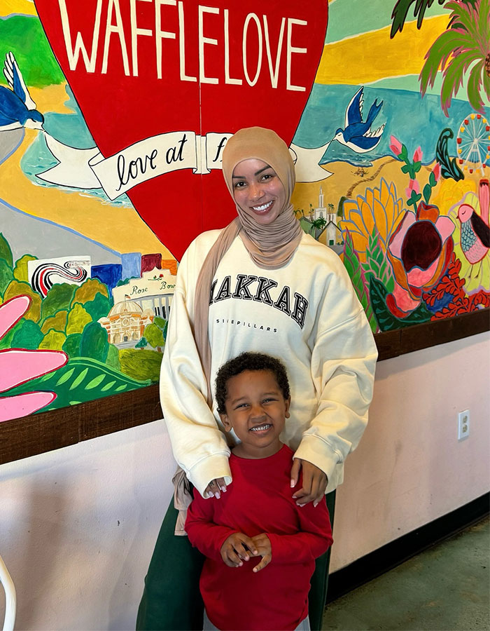 Woman wearing hijab and sweatshirt standing with child in front of colorful mural, highlighting cosplayed faith for a man topic. Woman wearing hijab and sweatshirt standing with child in front of colorful mural, highlighting cosplayed faith for a man topic.