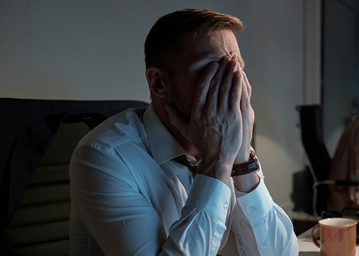 Stressed man in office holding face with hands, reflecting on not telling friend about getting fired situation.