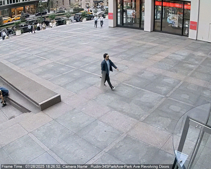Man walking alone on a large plaza outside a building with revolving doors in a busy urban area. Man walking alone on a large plaza outside a building with revolving doors in a busy urban area.