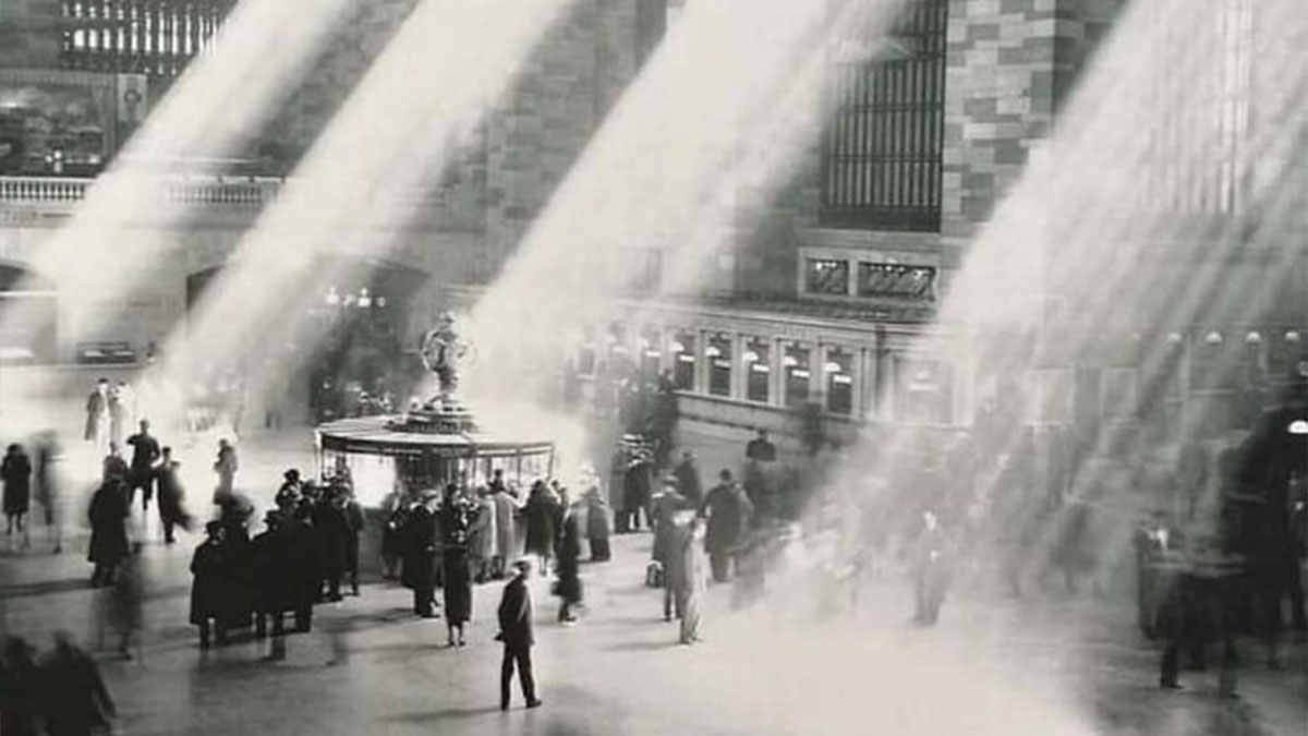 Old architecture interior with sunlight beams shining on people walking in a historic building lobby.