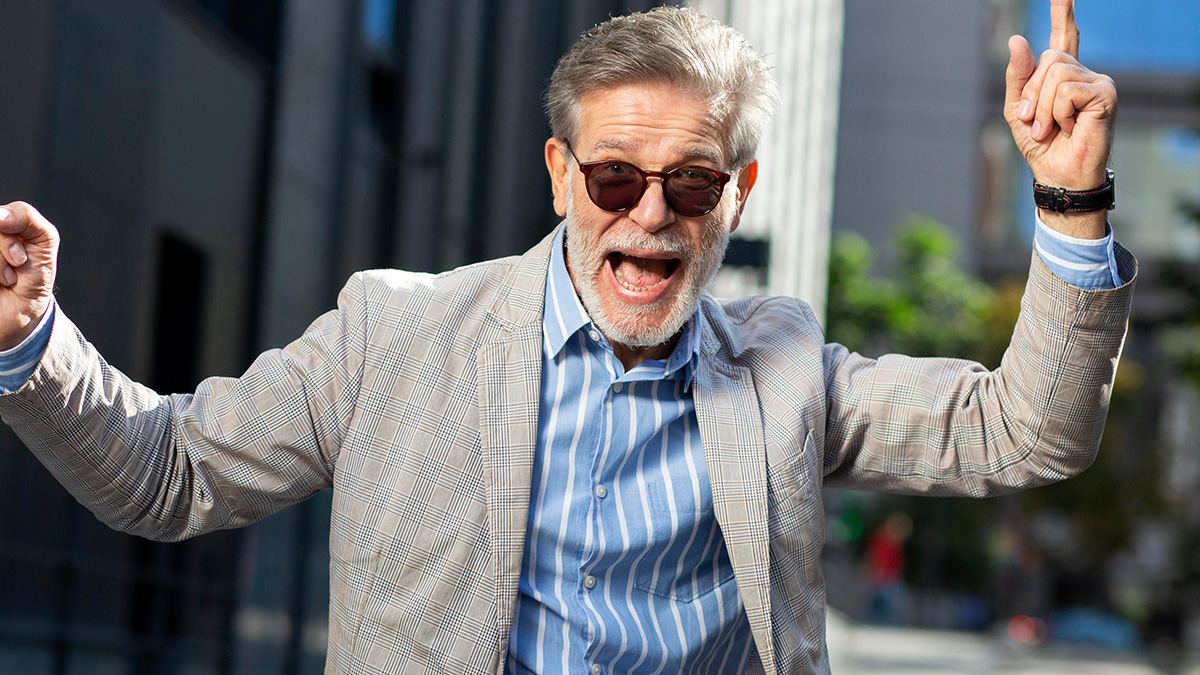 Energetic man in his 50s wearing sunglasses and a striped shirt, celebrating childfree lifestyle with no responsibility outdoors.