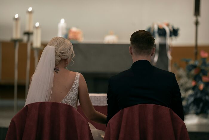 Bride and groom seated at altar during wedding ceremony with candles and floral decorations in background, student names concept.