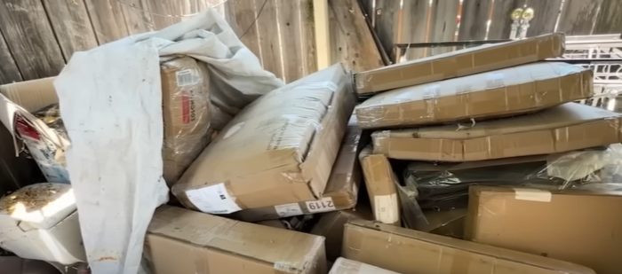 Large pile of Amazon packages mistakenly delivered to a woman’s home, stacked in a cluttered outdoor space. Large pile of Amazon packages mistakenly delivered to a woman’s home, stacked in a cluttered outdoor space.
