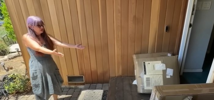 Woman with purple hair standing by multiple Amazon packages mistakenly delivered to her home over a year. Woman with purple hair standing by multiple Amazon packages mistakenly delivered to her home over a year.