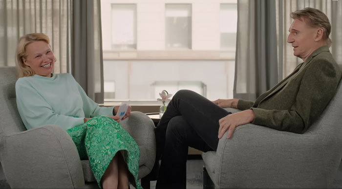 Pamela Anderson and Liam Neeson sitting in armchairs, smiling and engaged in a relaxed conversation indoors. Pamela Anderson and Liam Neeson sitting in armchairs, smiling and engaged in a relaxed conversation indoors.