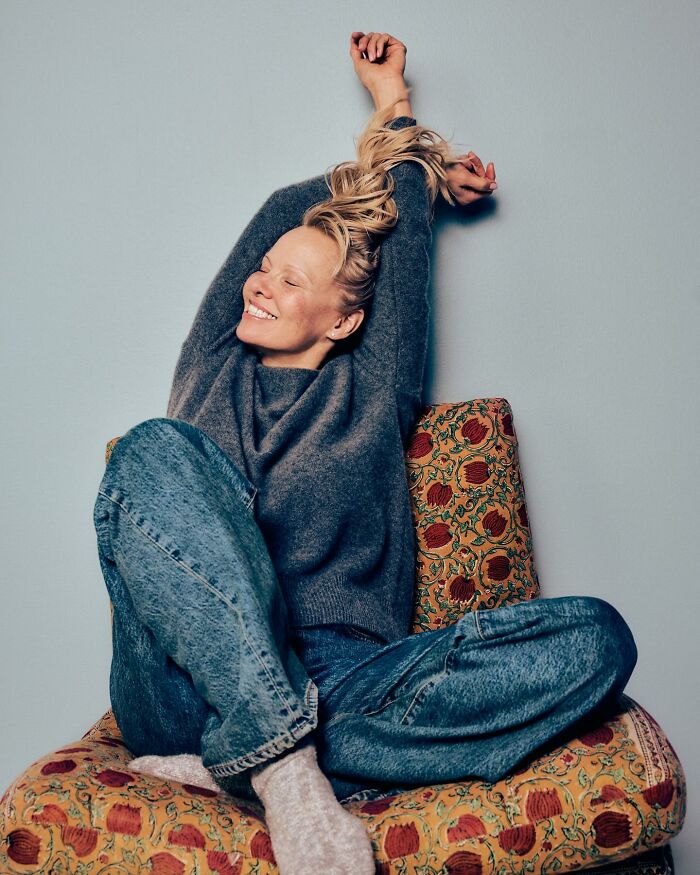 Smiling woman in casual sweater and jeans stretching while sitting on a patterned chair, reflecting Pamela Anderson dating Liam Neeson. Smiling woman in casual sweater and jeans stretching while sitting on a patterned chair, reflecting Pamela Anderson dating Liam Neeson.
