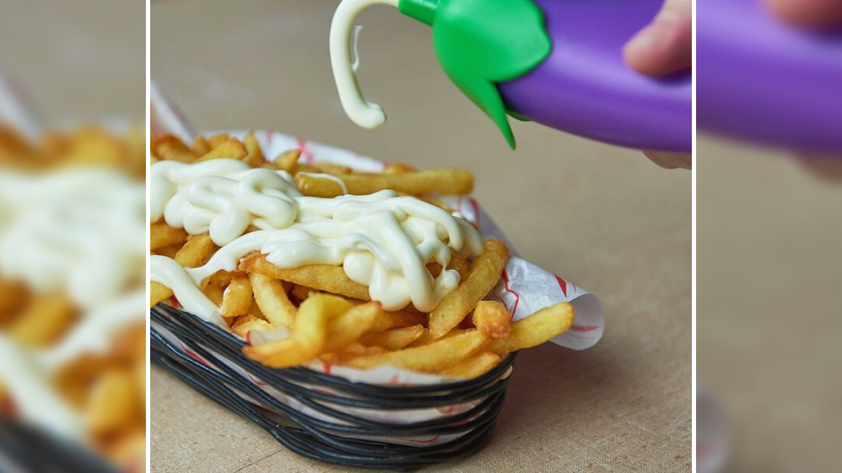 French fries topped with mayonnaise being squeezed from a purple kitchen item in a basket liner.