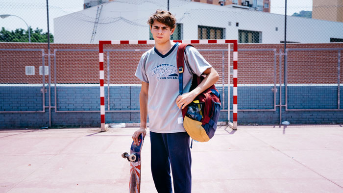 Teen boy holding skateboard and backpack on outdoor sports court, representing parents kid care and parenting. Teen boy holding skateboard and backpack on outdoor sports court, representing parents kid care and parenting.