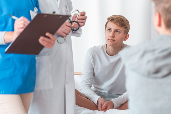 Teen boy sitting on medical bed listening to doctors discussing health care advice for parents kid care parenting. Teen boy sitting on medical bed listening to doctors discussing health care advice for parents kid care parenting.