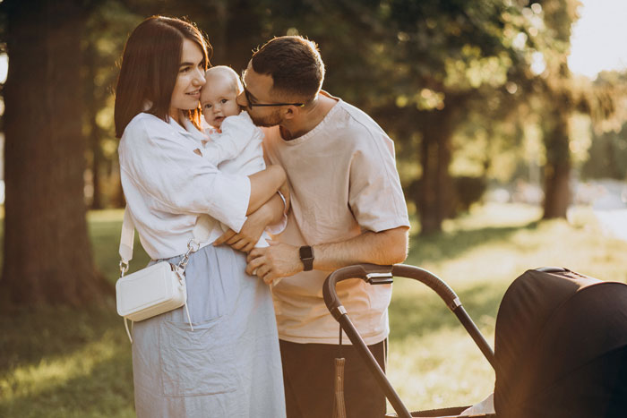 Young parents outdoors with baby and stroller, highlighting mom's overprotective feelings about in-laws helping with baby care. Young parents outdoors with baby and stroller, highlighting mom's overprotective feelings about in-laws helping with baby care.