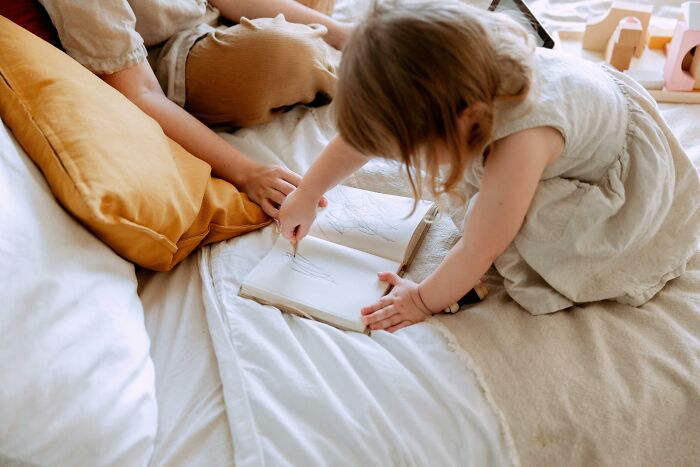 Toddler drawing in a notebook on bed with mother nearby, illustrating family and home ownership issues. Toddler drawing in a notebook on bed with mother nearby, illustrating family and home ownership issues.