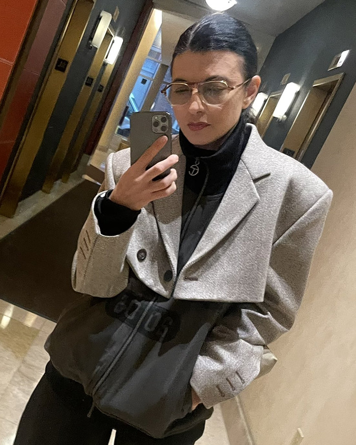 Woman wearing glasses and a grey blazer taking a mirror selfie, related to Pedro Pascal cutting ties with stylist controversy. Woman wearing glasses and a grey blazer taking a mirror selfie, related to Pedro Pascal cutting ties with stylist controversy.