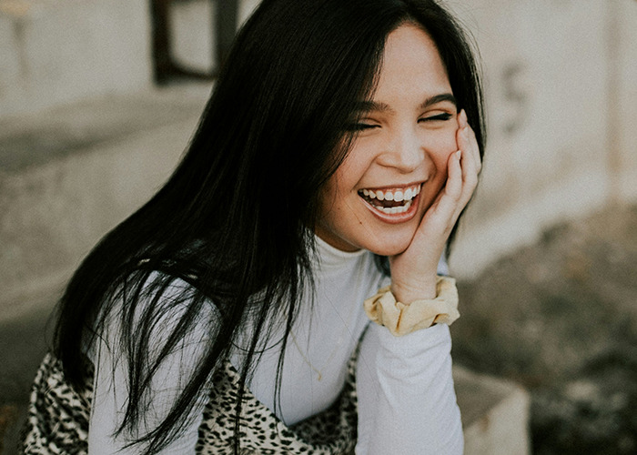 Young woman laughing joyfully outdoors, capturing a candid moment of savage insults shared by 80 people.