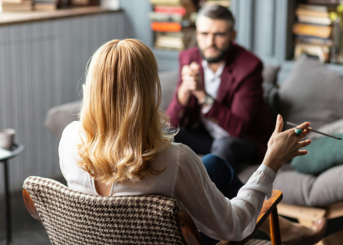 Woman gesturing with pen while talking to a bearded man, illustrating conversation about savage insults.