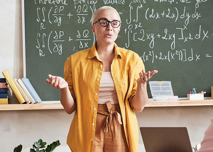 Woman in glasses teaching complex math equations in front of blackboard, illustrating savage insults with confident expression.