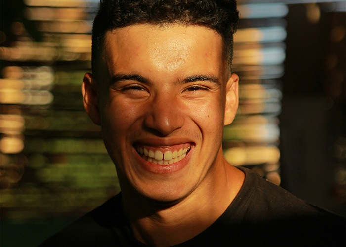 Young man smiling brightly in natural light, capturing a moment of joy and confidence in a casual setting for savage insults content.