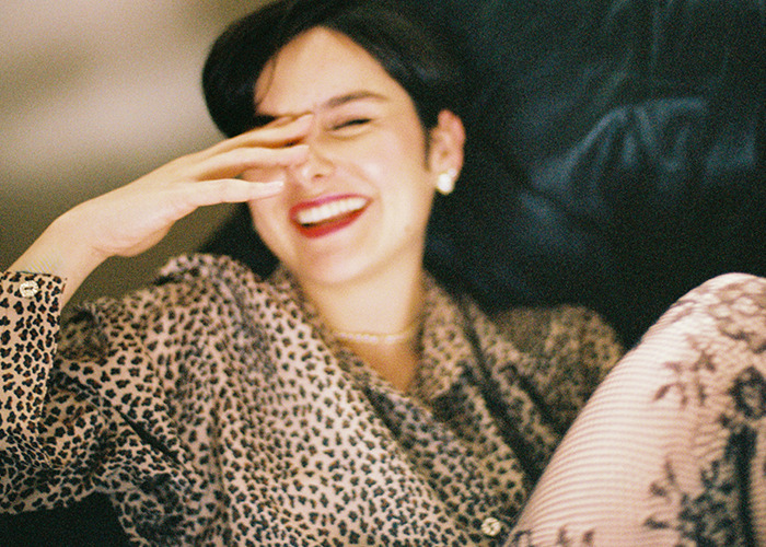 Young woman laughing and covering her face while sitting on a couch, illustrating reactions to savage insults shared online.