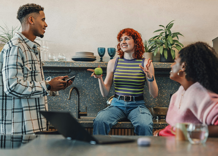 Three friends having a lively conversation in a modern kitchen, sharing savage insults and jokes with smiles.