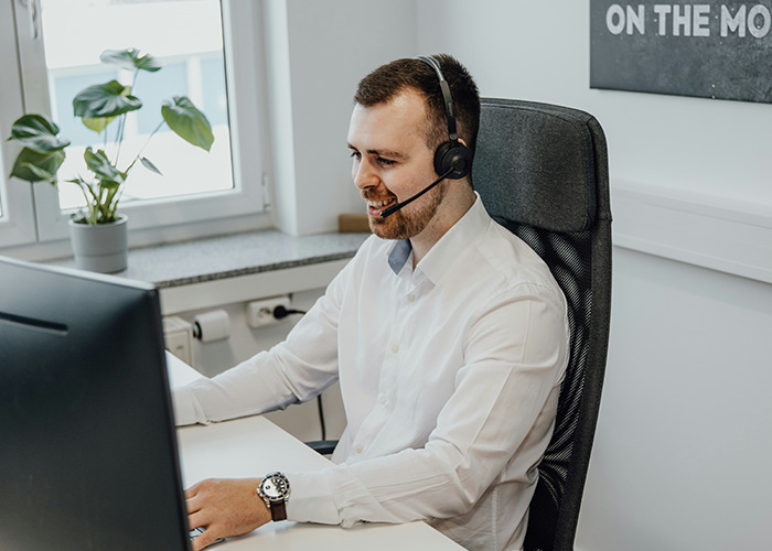 Man wearing headset and white shirt smiling while working at computer, illustrating savage insults shared online.